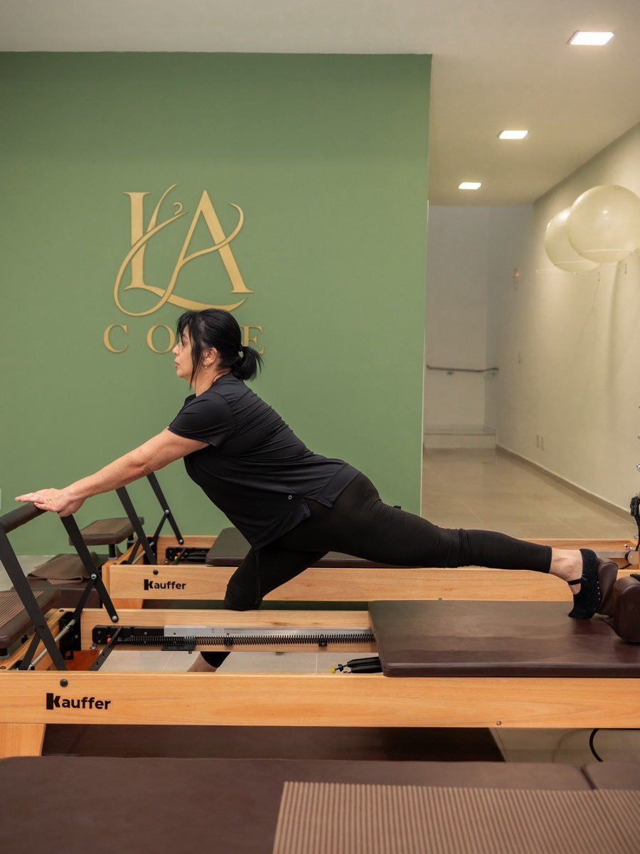 Aluna alongando no Reformer, com o logo da LA Core na parede verde ao fundo