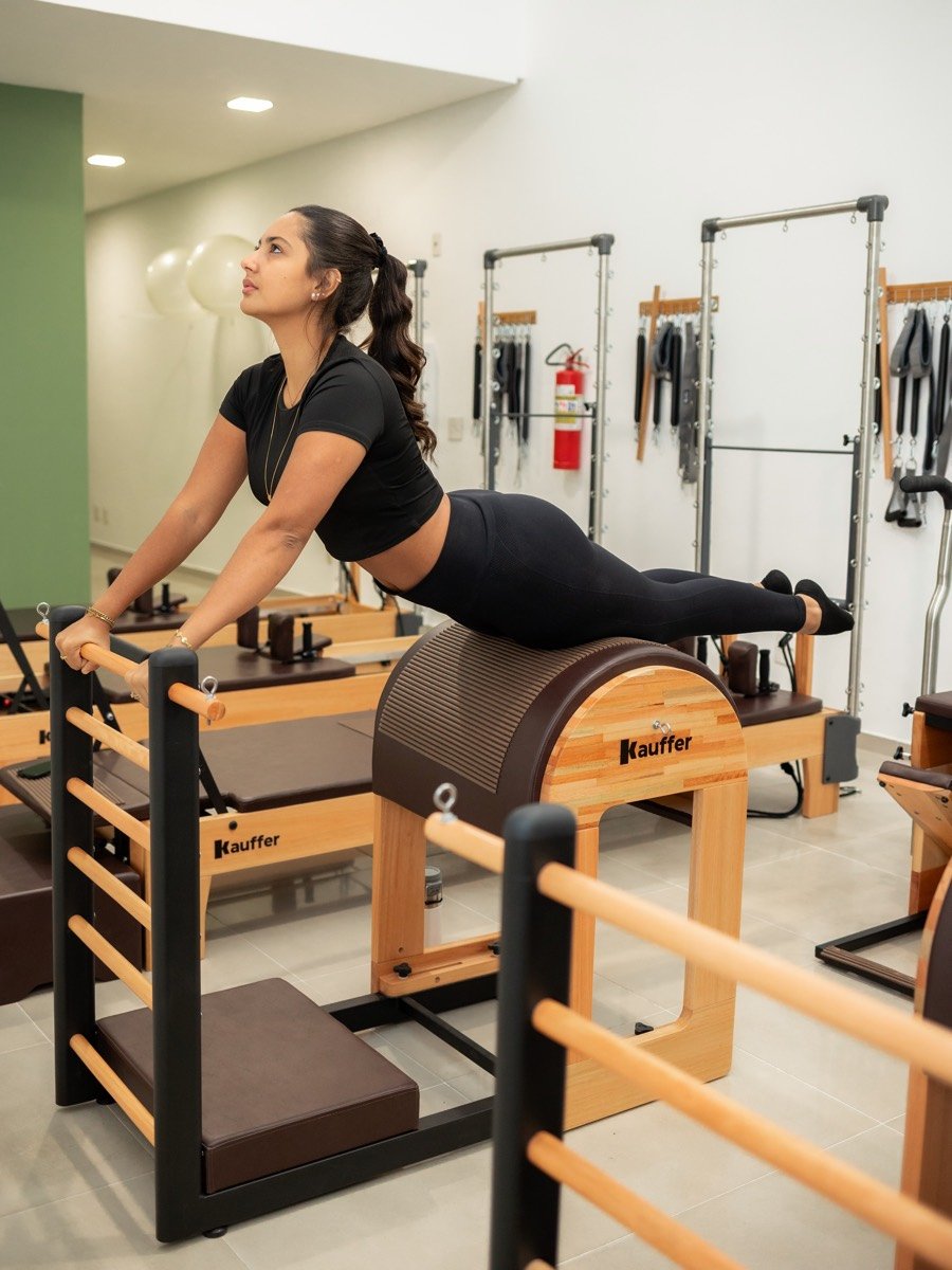 Aluna fazendo exercício no Ladder Barrel, com aparelhos de parede e bolas suíças ao fundo